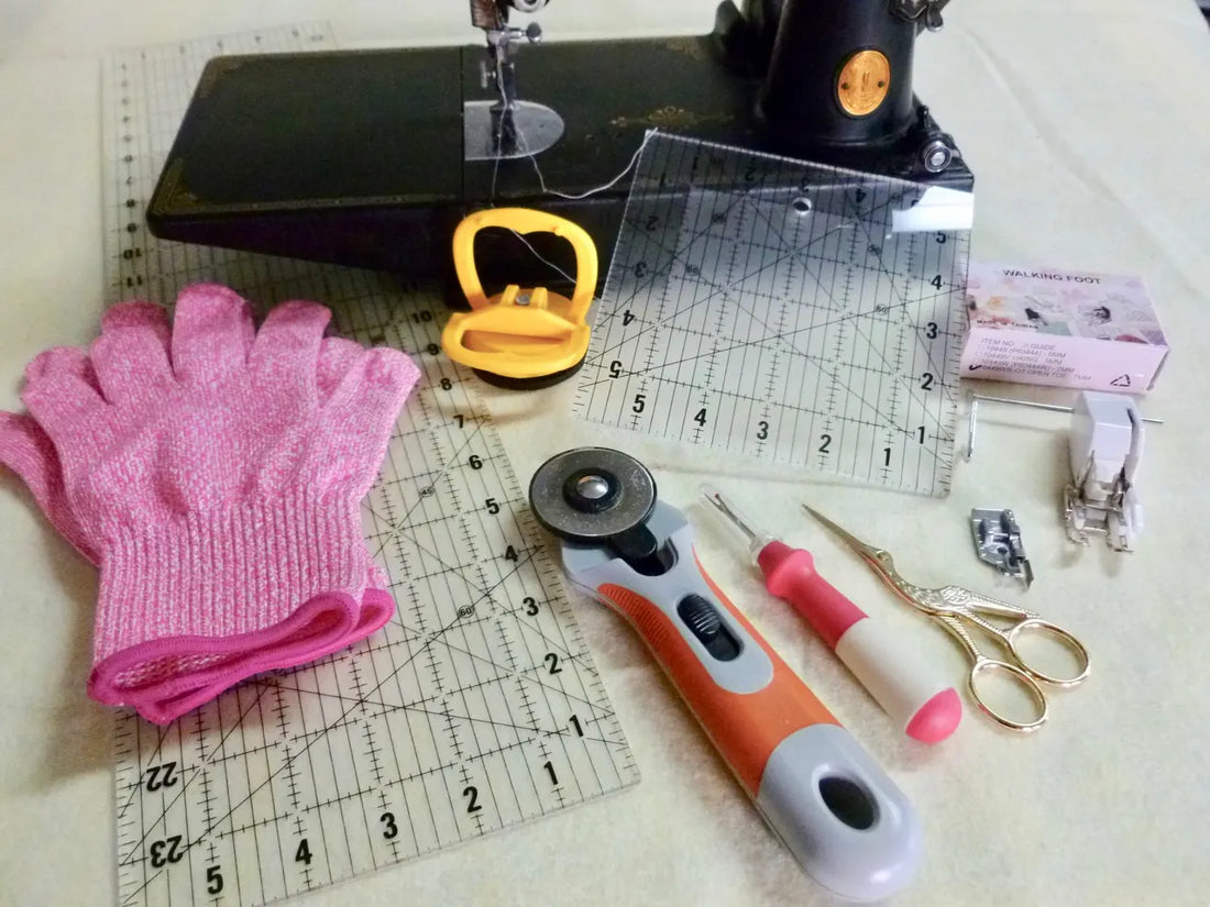 Beginner quilting tools laid out including a rotary cutter, acrylic quilting rulers, seam ripper, thread snips, quilting gloves, and a walking foot on a sewing machine.